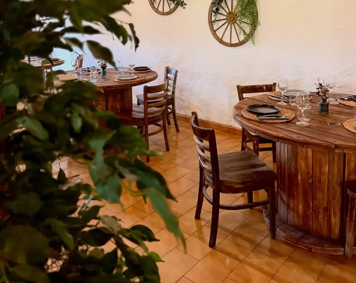 Comedor de estilo rústico con mesas, sillas y vajilla de madera sobre suelo de baldosas.