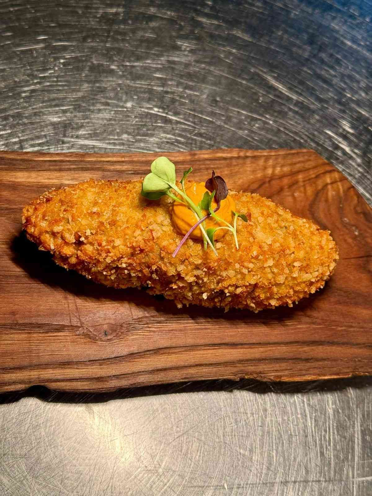 Croqueta frita empanizada sobre una tabla de madera, cubierta con microvegetales.