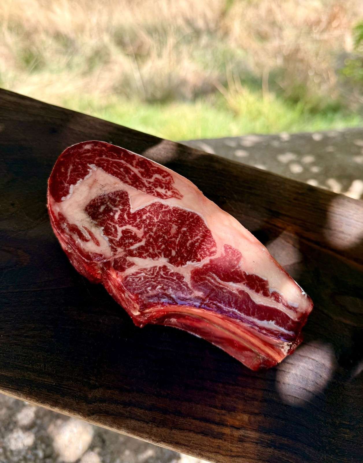 Filete de ternera cruda veteada sobre una superficie de madera al aire libre.