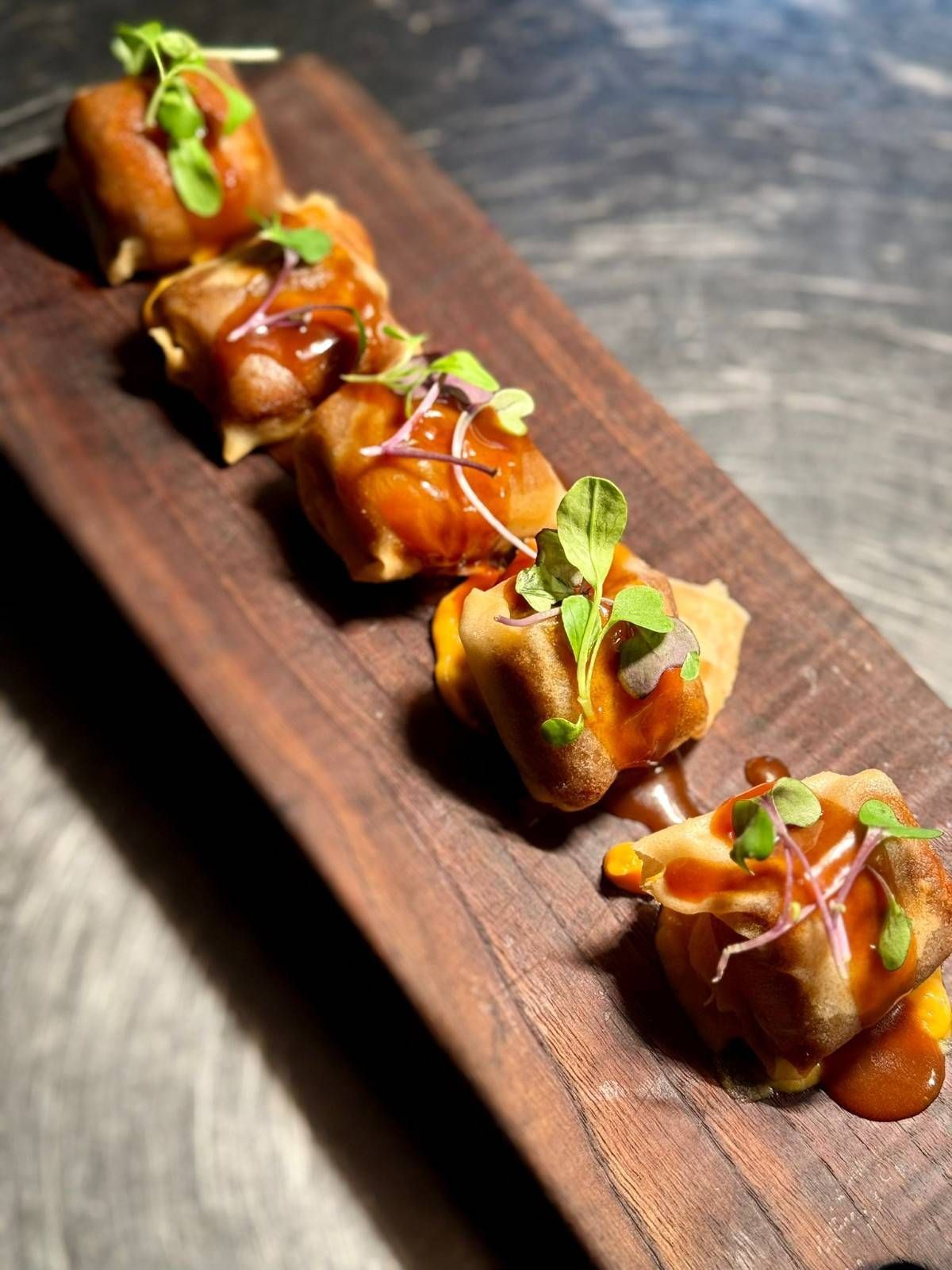 Bocaditos glaseados servidos en una tabla de madera, adornados con hierbas.