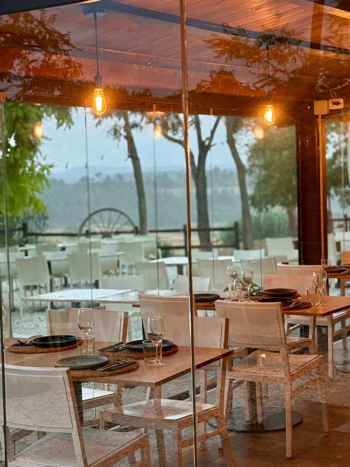 Comedor de restaurante moderno con mesas y sillas blancas, iluminación cálida y vista al mar a través de grandes ventanales.