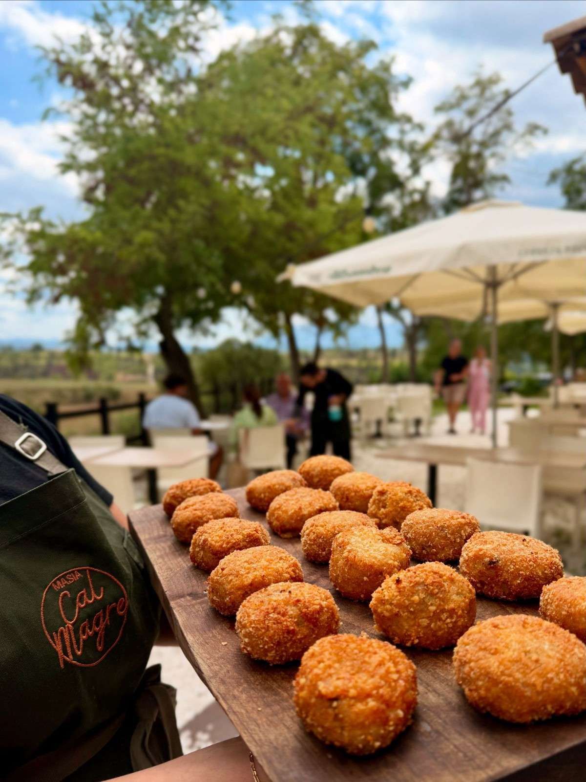 Bandeja de bocadillos fritos dorados sobre una mesa al aire libre bajo una sombrilla de patio soleada.