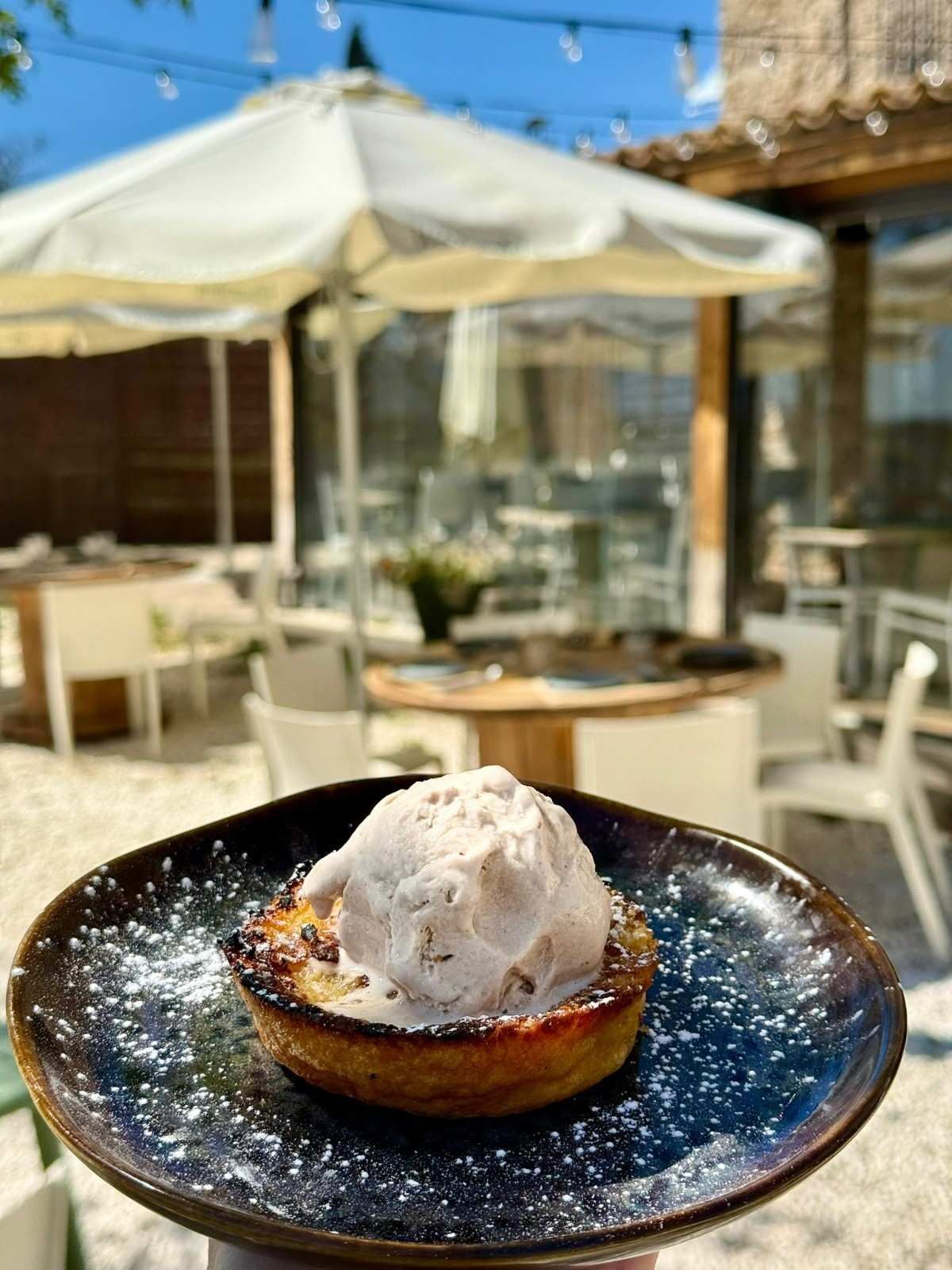 Tarta de postre cubierta con helado de vainilla en un plato negro en una soleada terraza de un café.