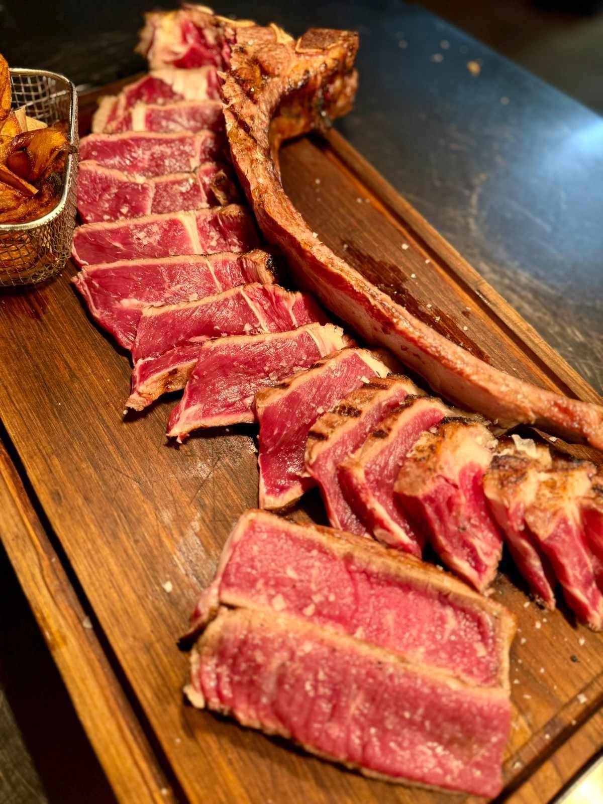 Filete poco hecho en rodajas sobre una tabla de madera con sal gruesa y una pequeña salsa.