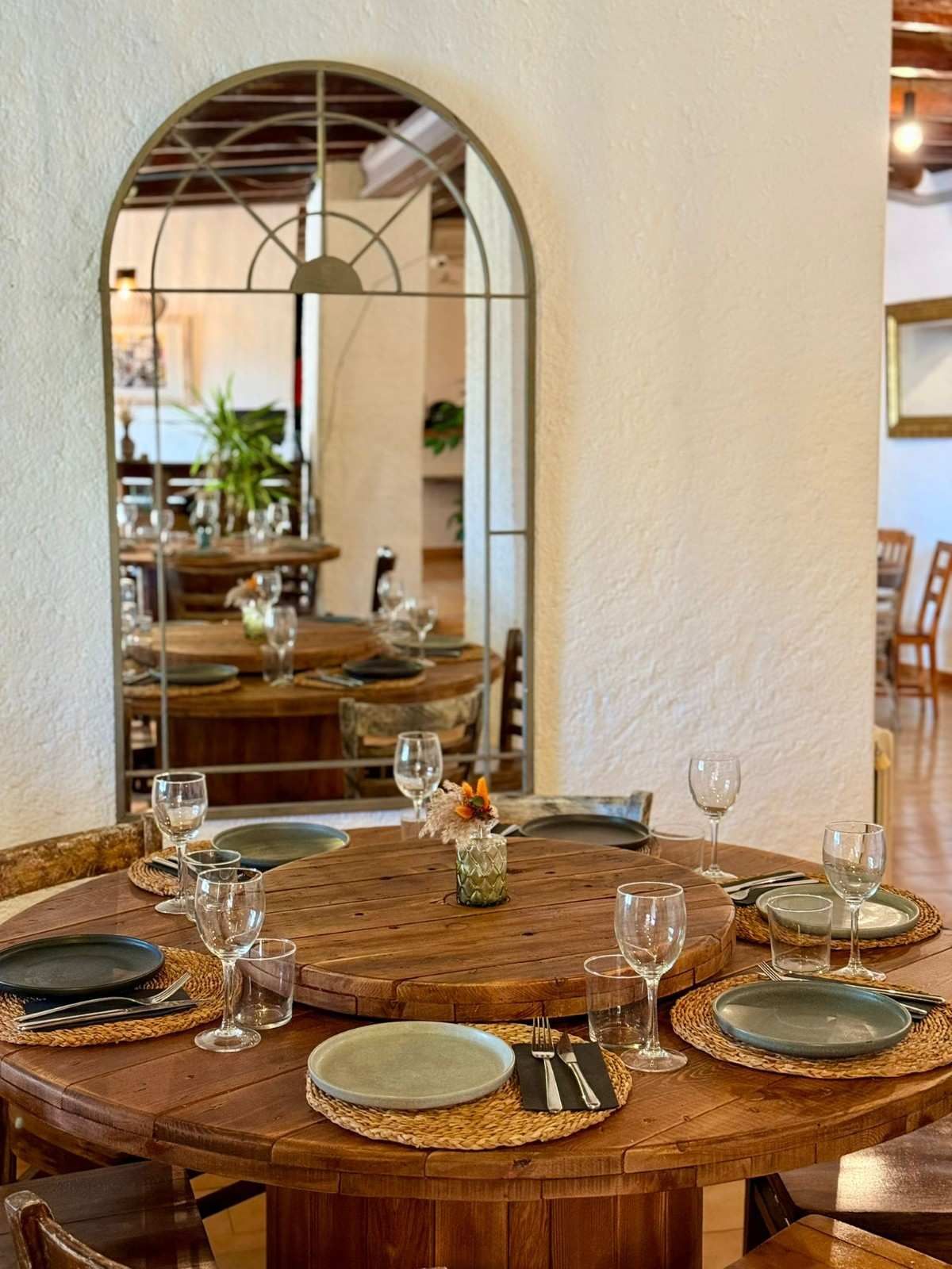 Juego de mesa de comedor rústico con platos y vasos bajo un espejo de pared arqueado.
