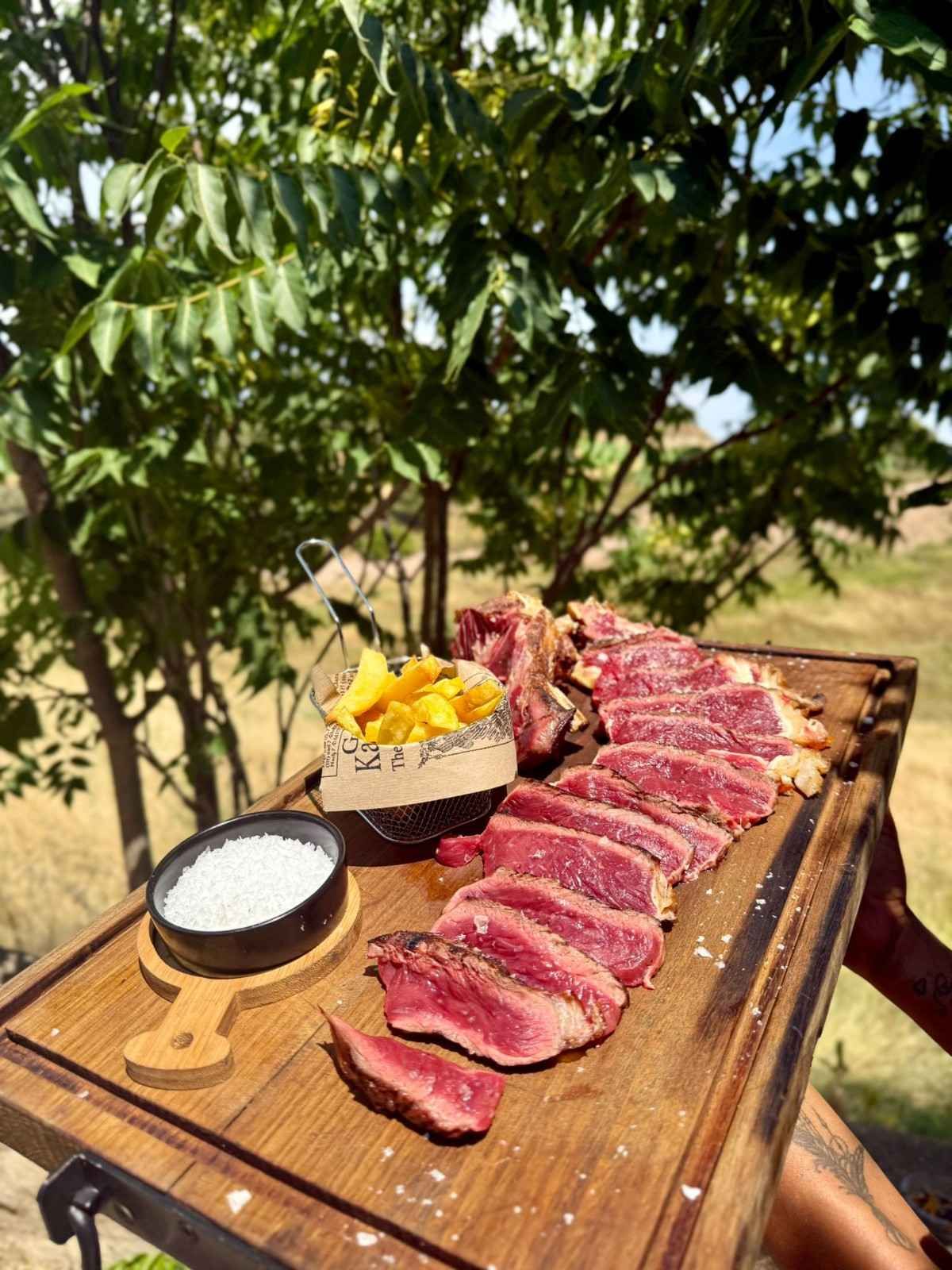 Filete a la parrilla en una tabla de madera con salsas, al aire libre bajo un árbol.