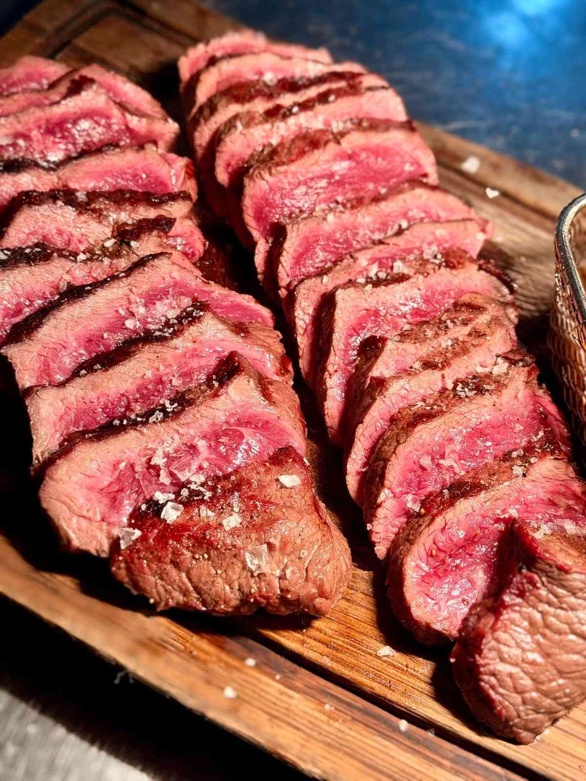 Filete poco hecho en rodajas sobre una tabla de cortar de madera, con la corteza dorada y el centro rosado.