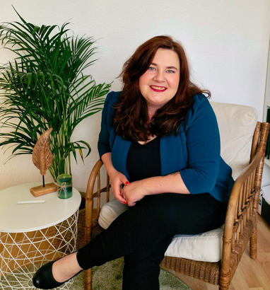 Eine Frau mit einer schwarzen Jacke und einer Halskette lächelt in die Kamera.