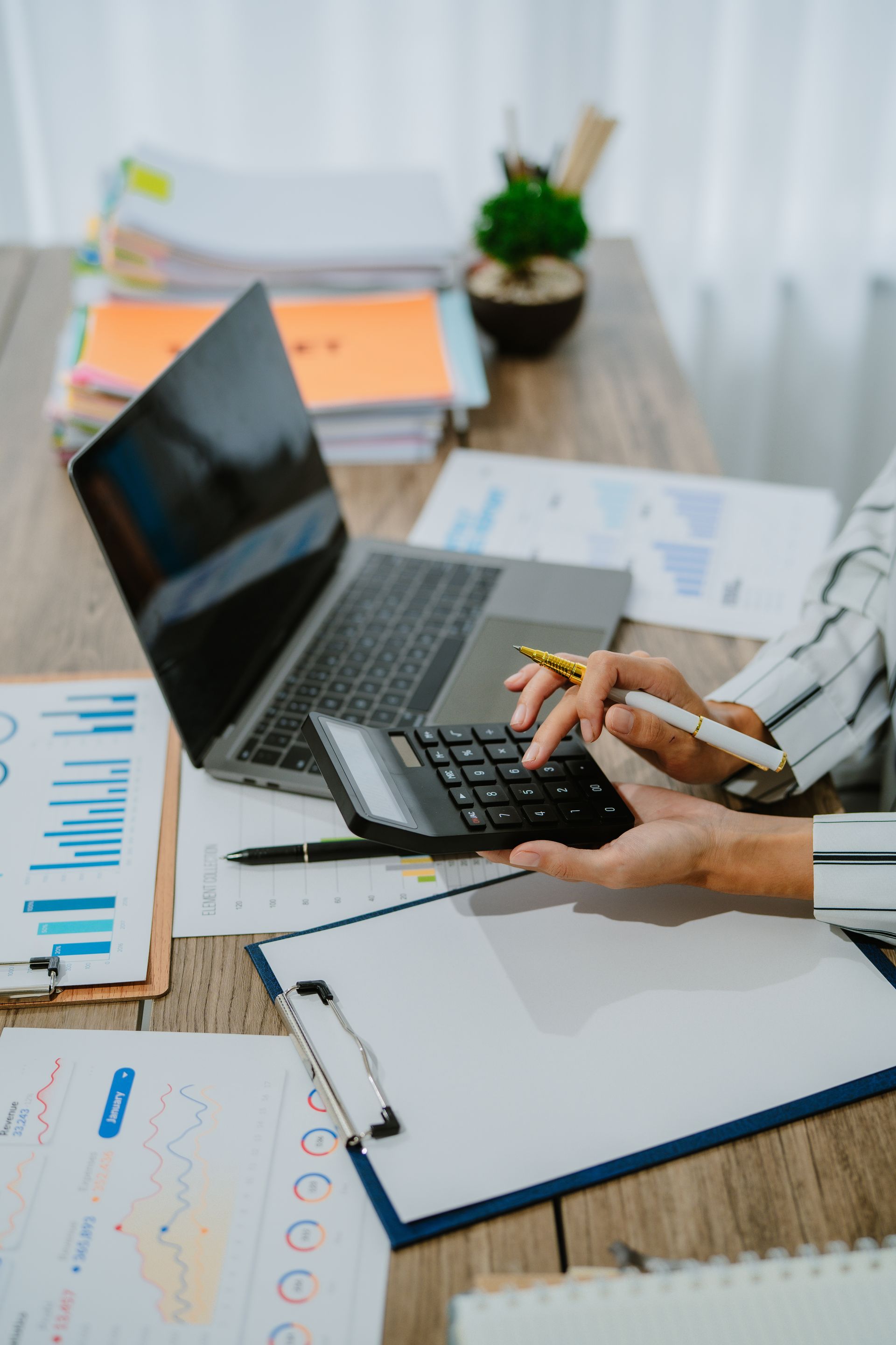 Une personne utilise une calculatrice et un ordinateur portable à un bureau où sont posés des documents financiers.