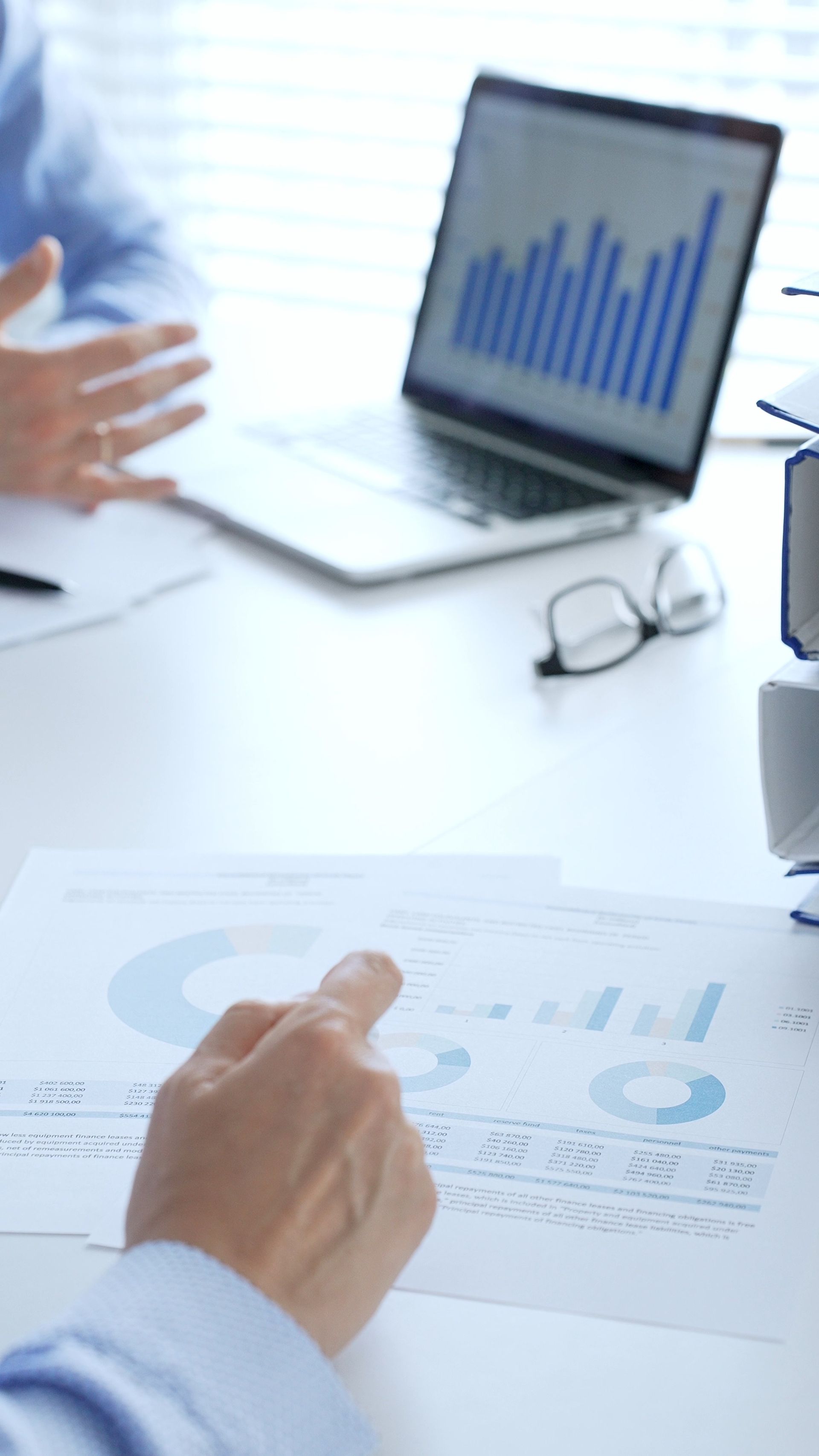 Une personne désigne un graphique, un ordinateur portable affiche un graphique à barres, et discute de données financières dans un bureau.