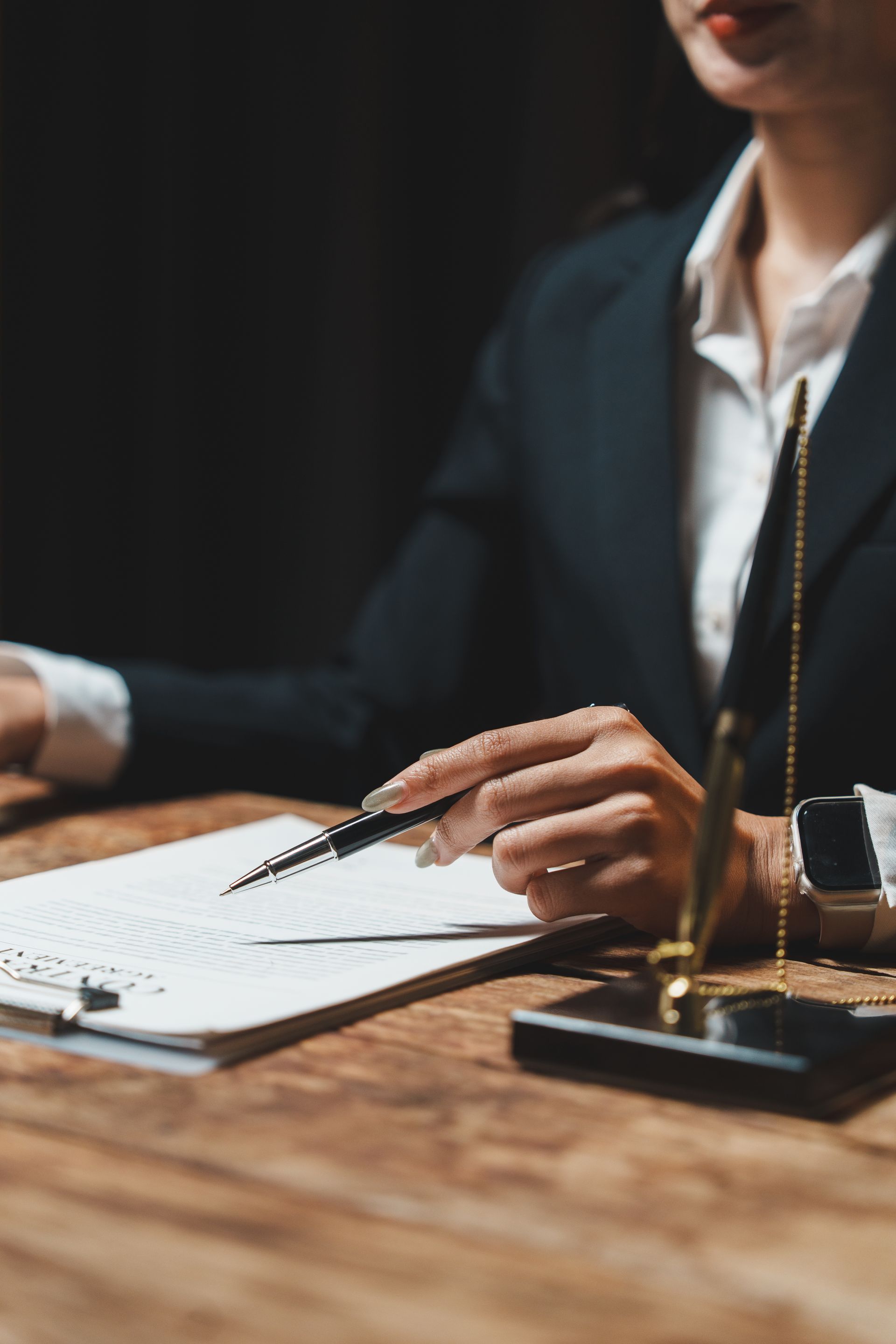 Une personne en costume pointe un stylo vers un document posé sur un bureau en bois.