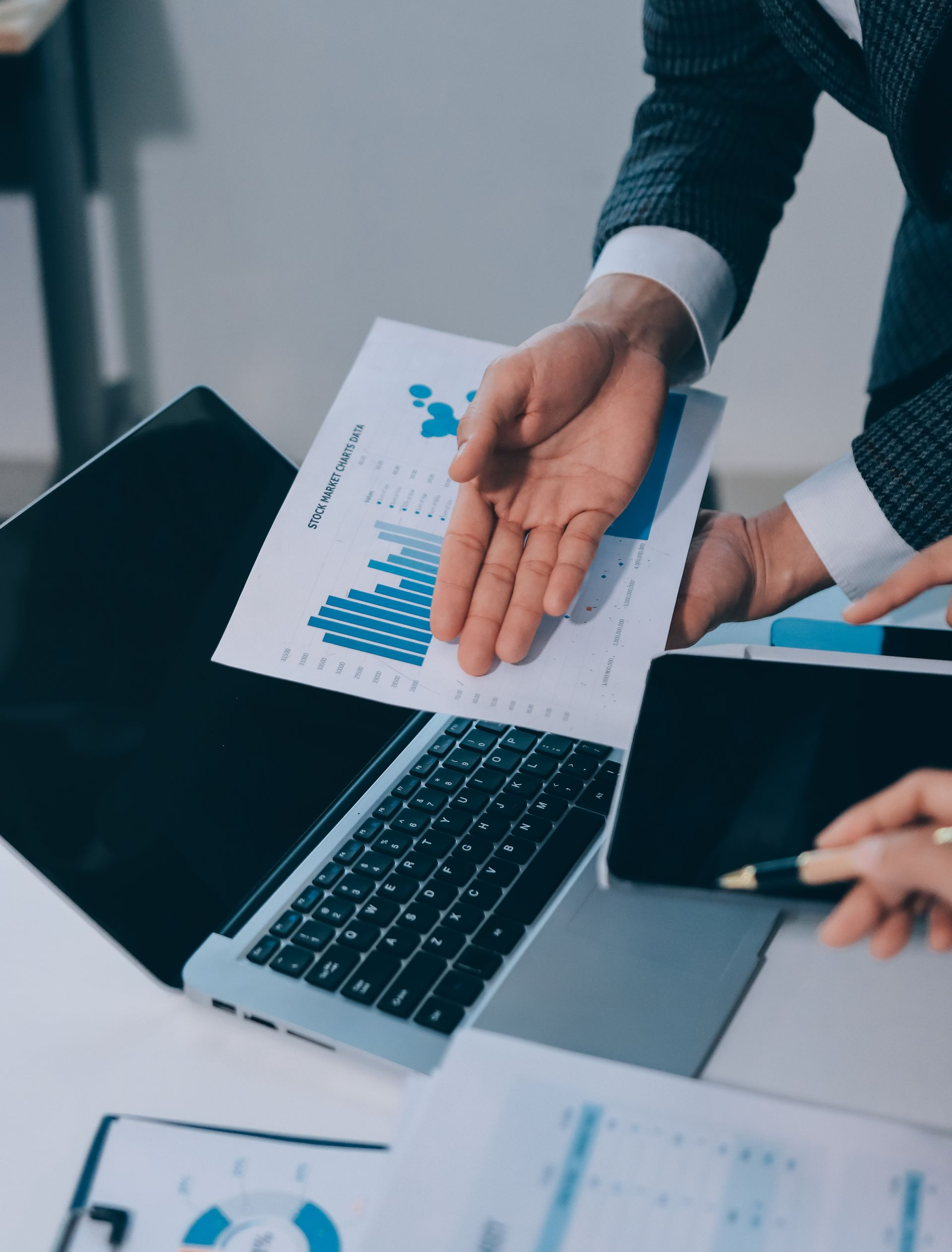 Une personne désigne du doigt un graphique comportant des courbes bleues, près d'un ordinateur portable et d'une tablette, probablement dans un bureau.