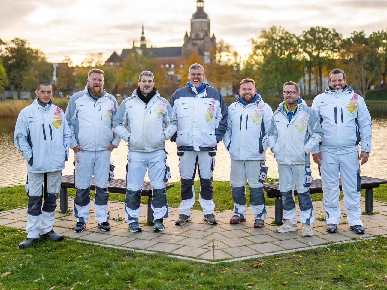 Eine Gruppe von Männern steht nebeneinander vor einem See.