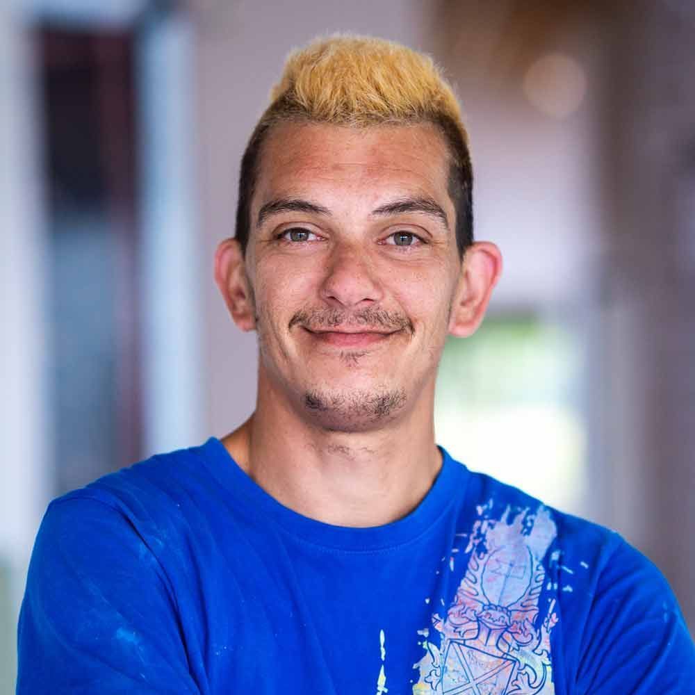 Ein Mann mit blondem Haar trägt ein blaues Hemd und lächelt.