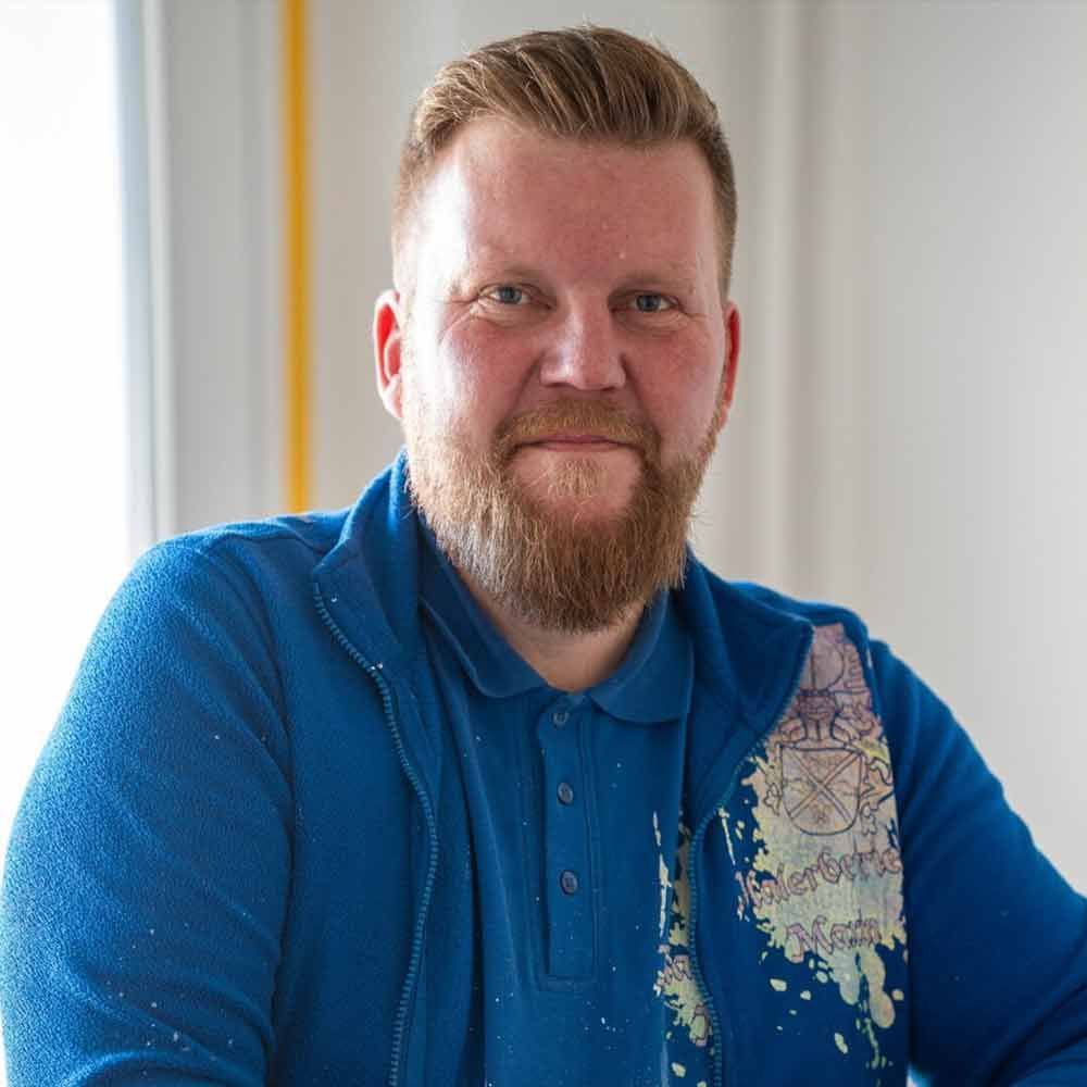 Ein Mann mit Bart trägt ein blaues Hemd und eine blaue Jacke.