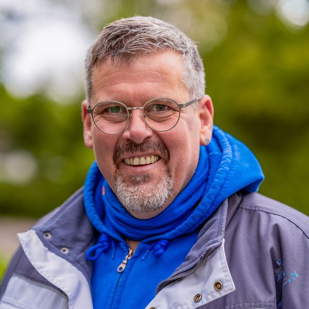 Ein Mann mit Brille und blauem Schal lächelt in die Kamera.