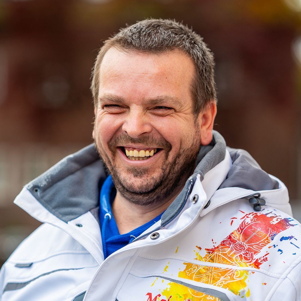 Ein Mann in einer weißen Jacke mit einem Red Bull-Logo lächelt.
