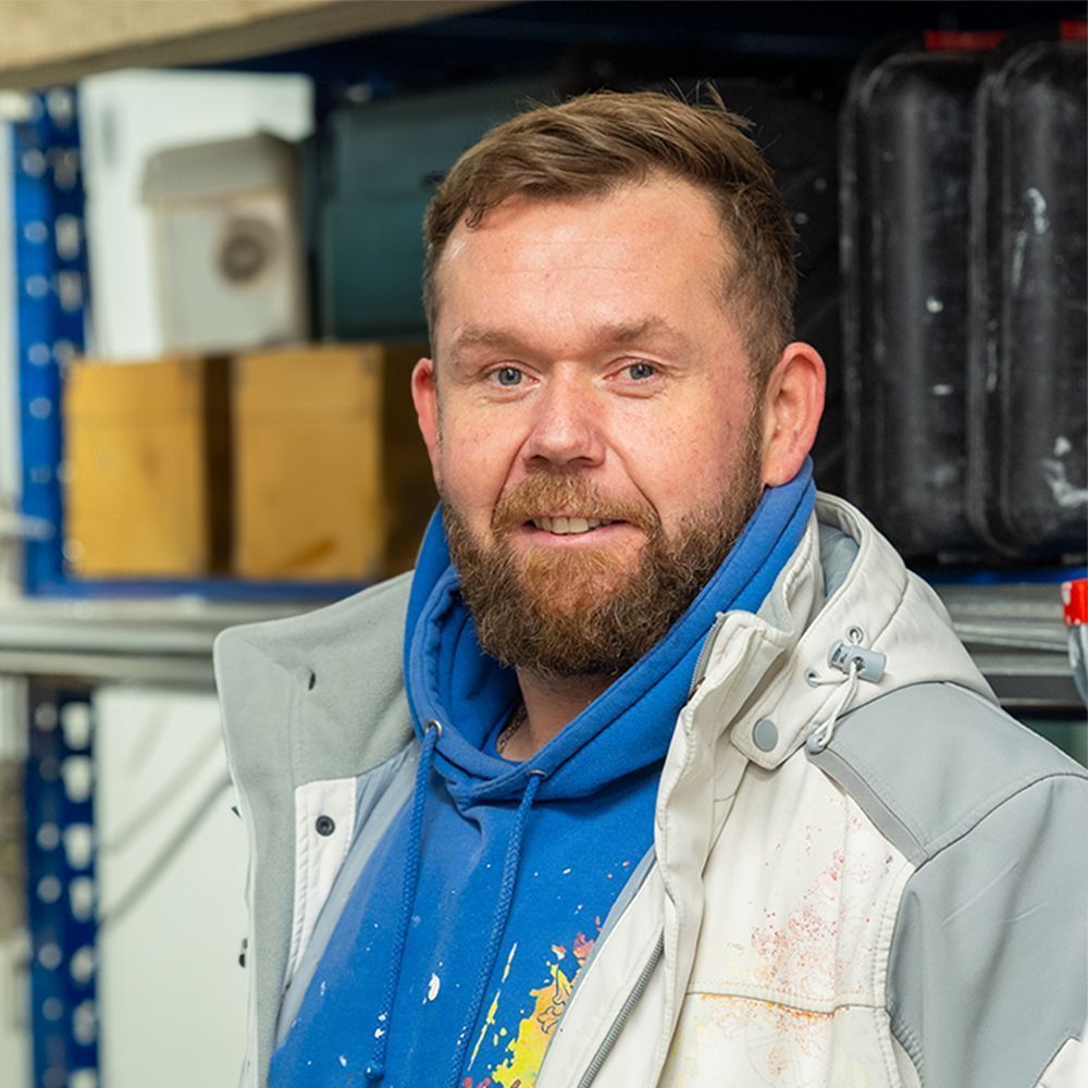Ein Mann mit Bart trägt einen blauen Kapuzenpullover und eine weiße Jacke.