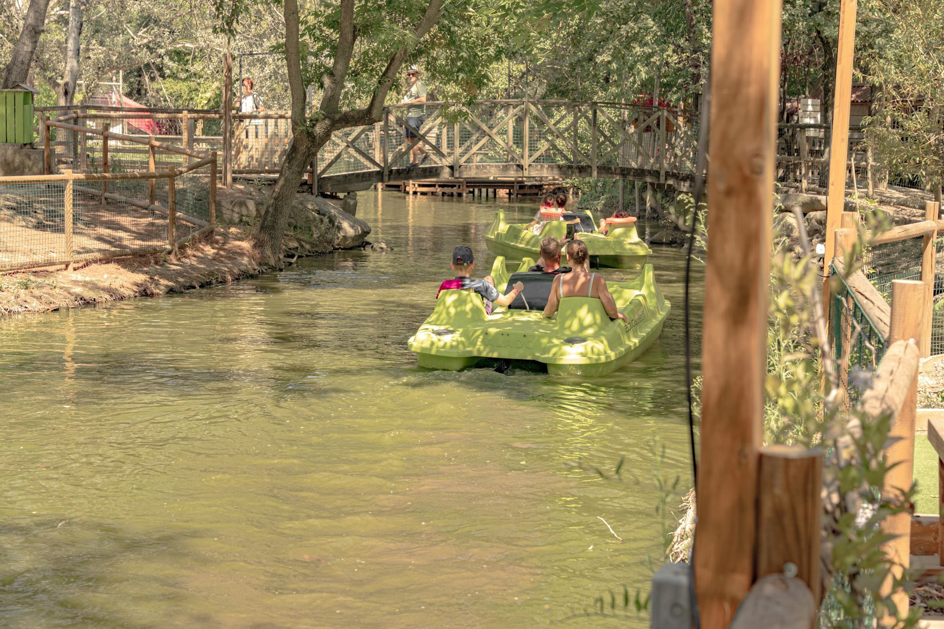 Deux barques à aubes vert clair avec des personnes sur un canal ; pont en bois et clôture tout autour.