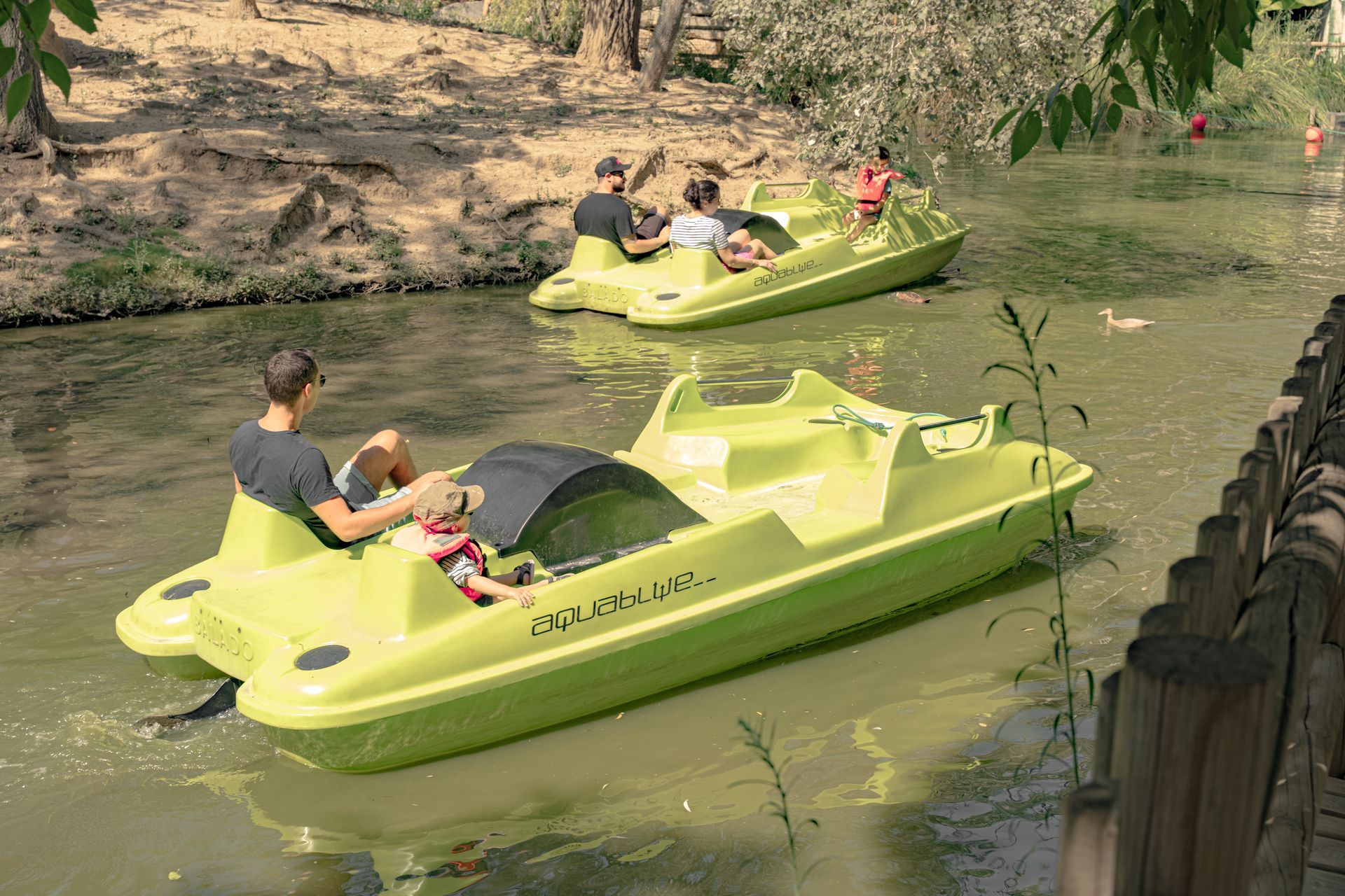 Deux pédalos vert clair avec des personnes sur un cours d'eau.