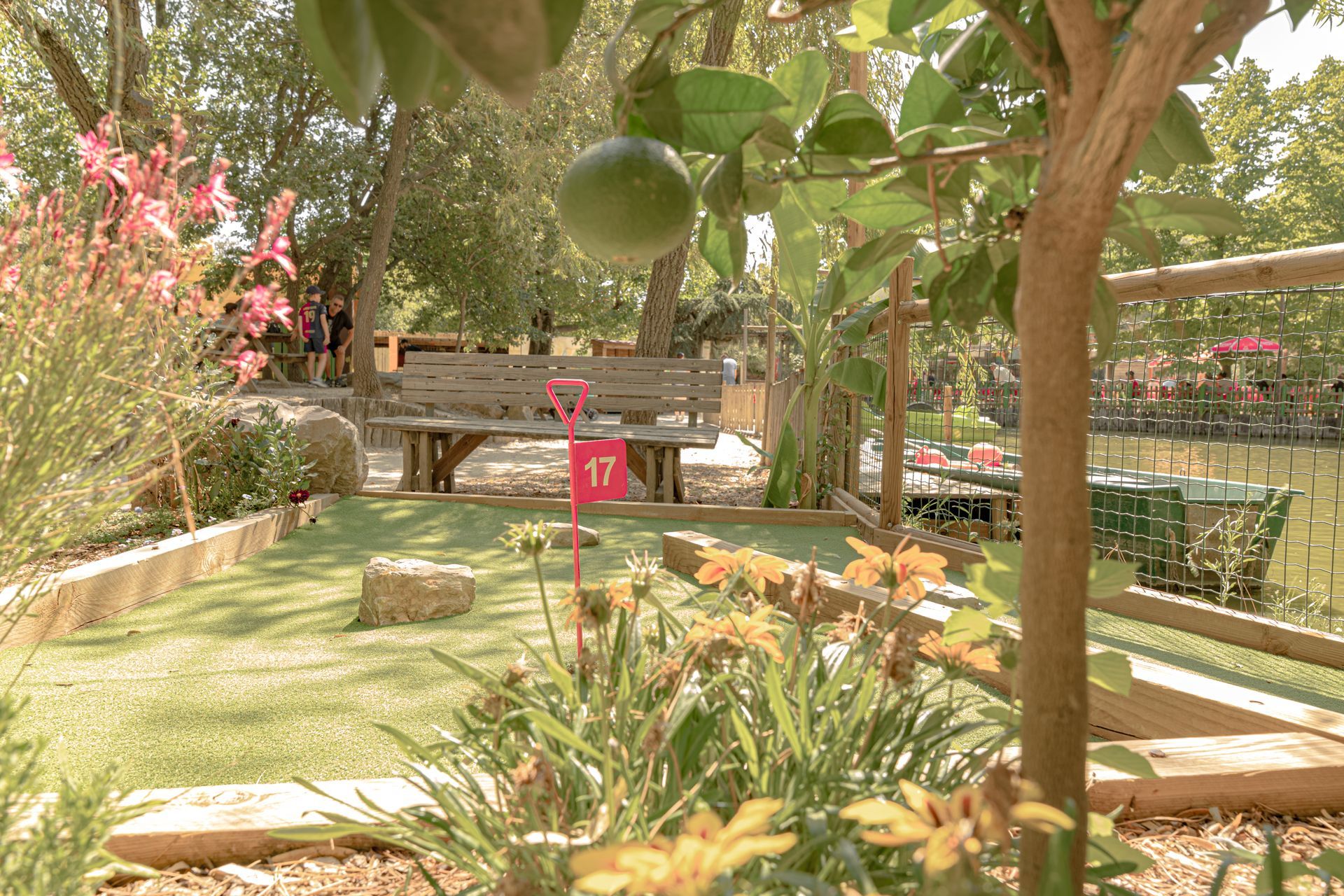 Scène de minigolf avec gazon vert, marqueur flamant rose, banc et feuillage.