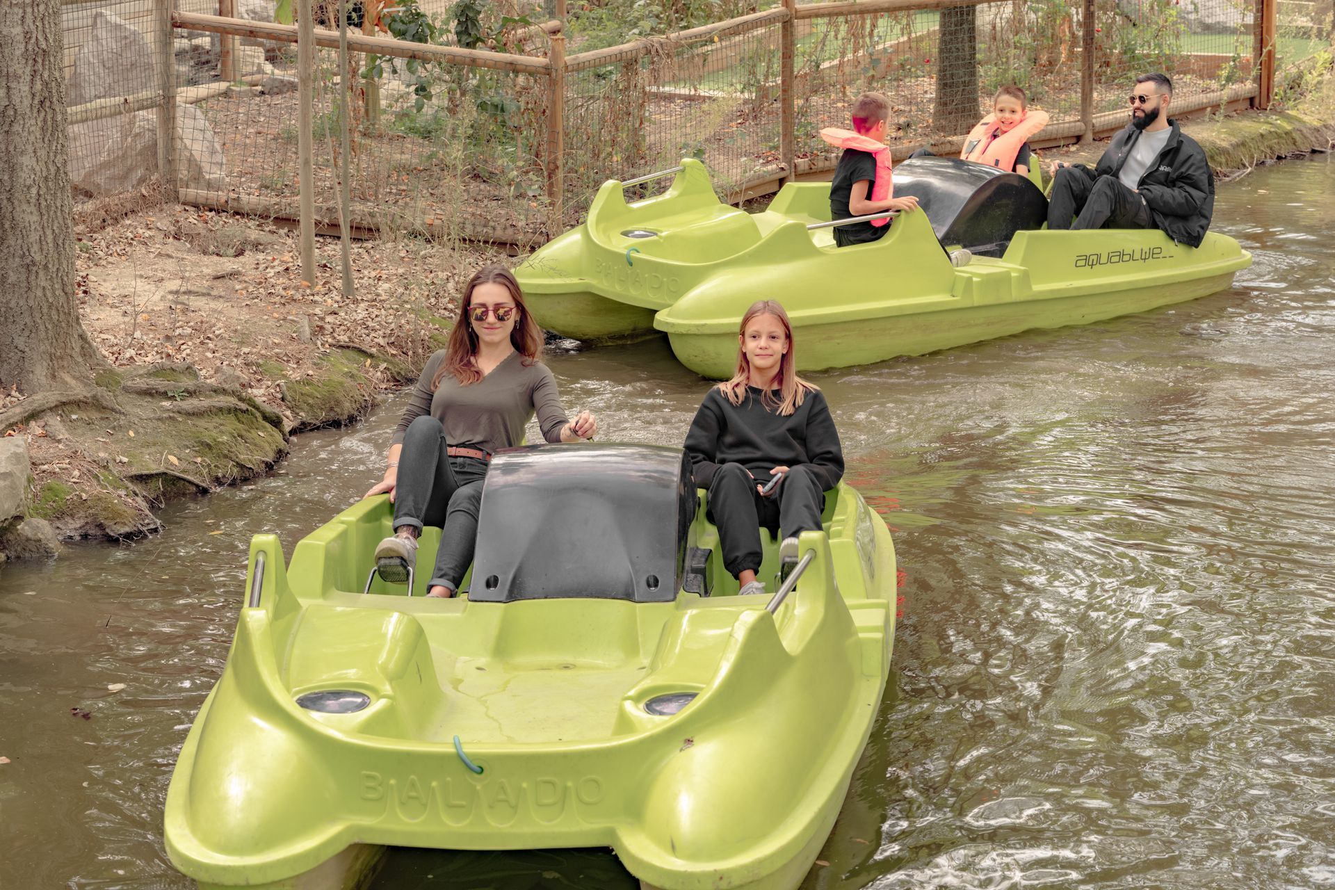 Des personnes naviguent en pédalo vert sur un cours d'eau bordé d'arbres.