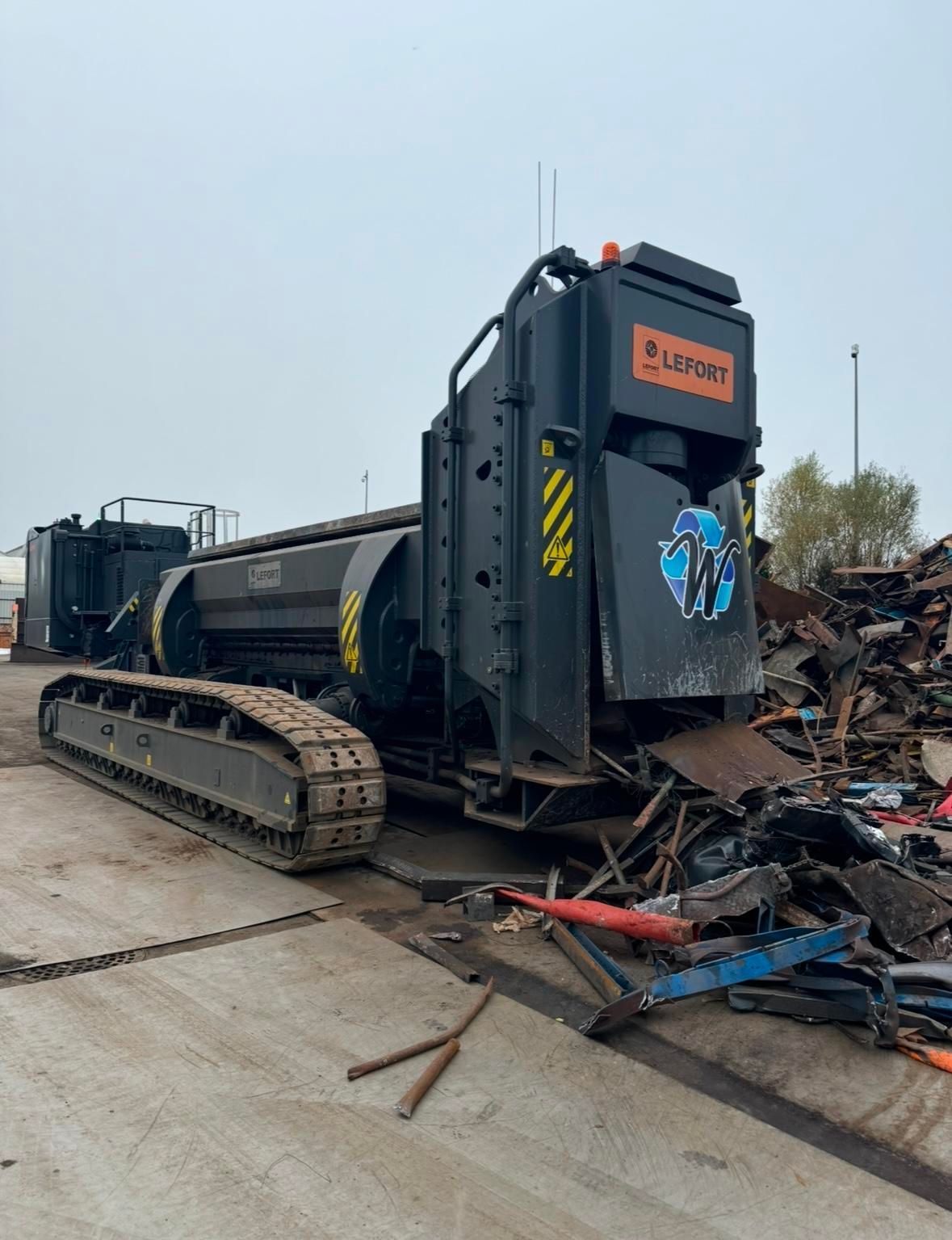 Véhicule imposant sur chenille devant des déchets métalliques.