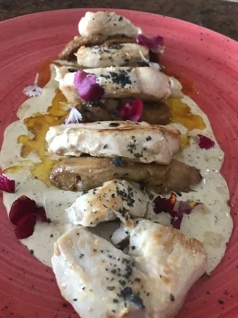 Postre en capas emplatado con glaseado de crema, semillas negras y pétalos de flores rosas sobre un plato rojo.