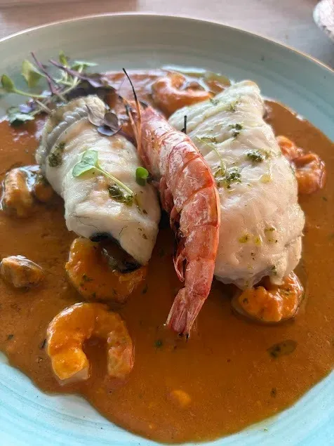 Plato de mariscos con filetes de pescado, camarones y salsa en un plato blanco.