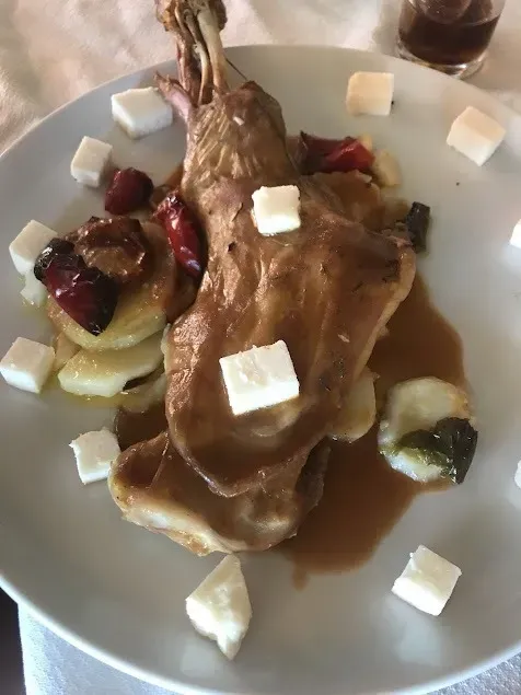 Carne asada con salsa en un plato blanco, cubierta con cubos de queso y servida con verduras rojas y verdes.