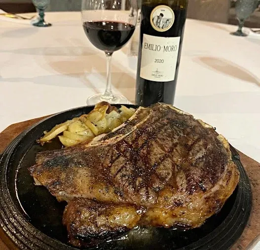 Filete a la parrilla en un plato con papas fritas y una copa de vino tinto en una mesa de comedor.