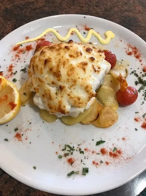 Plato de marisco al horno con salsa cremosa, servido en un plato blanco y adornado con hierbas aromáticas y tomates cherry.