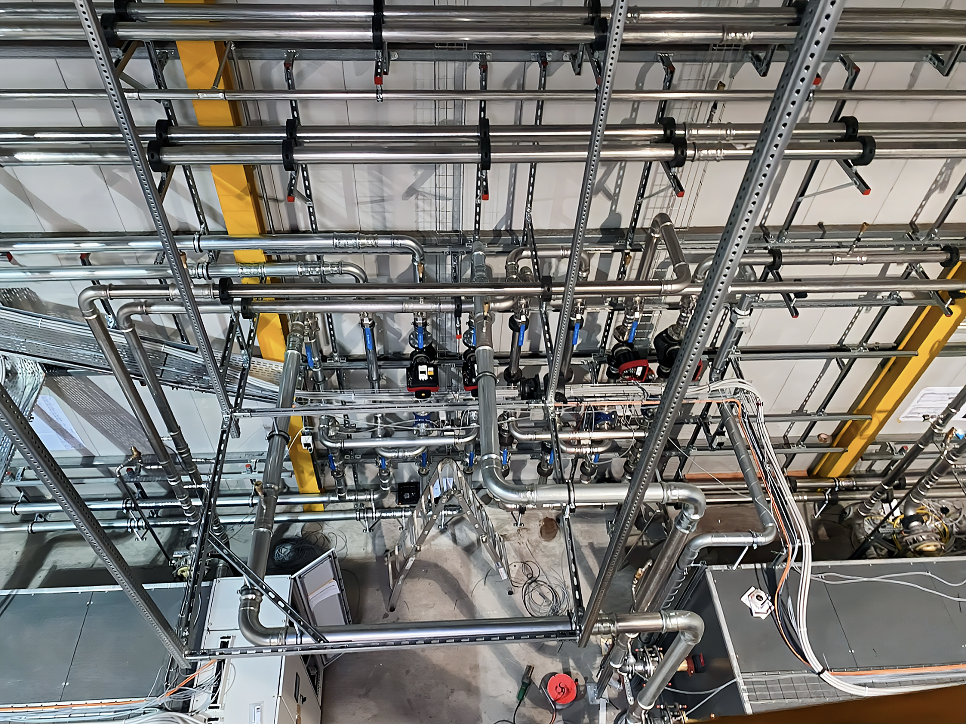 In einer industriellen Umgebung ist eine Kabelrinne aus Metalldraht auf blauen Trägerkonstruktionen montiert.