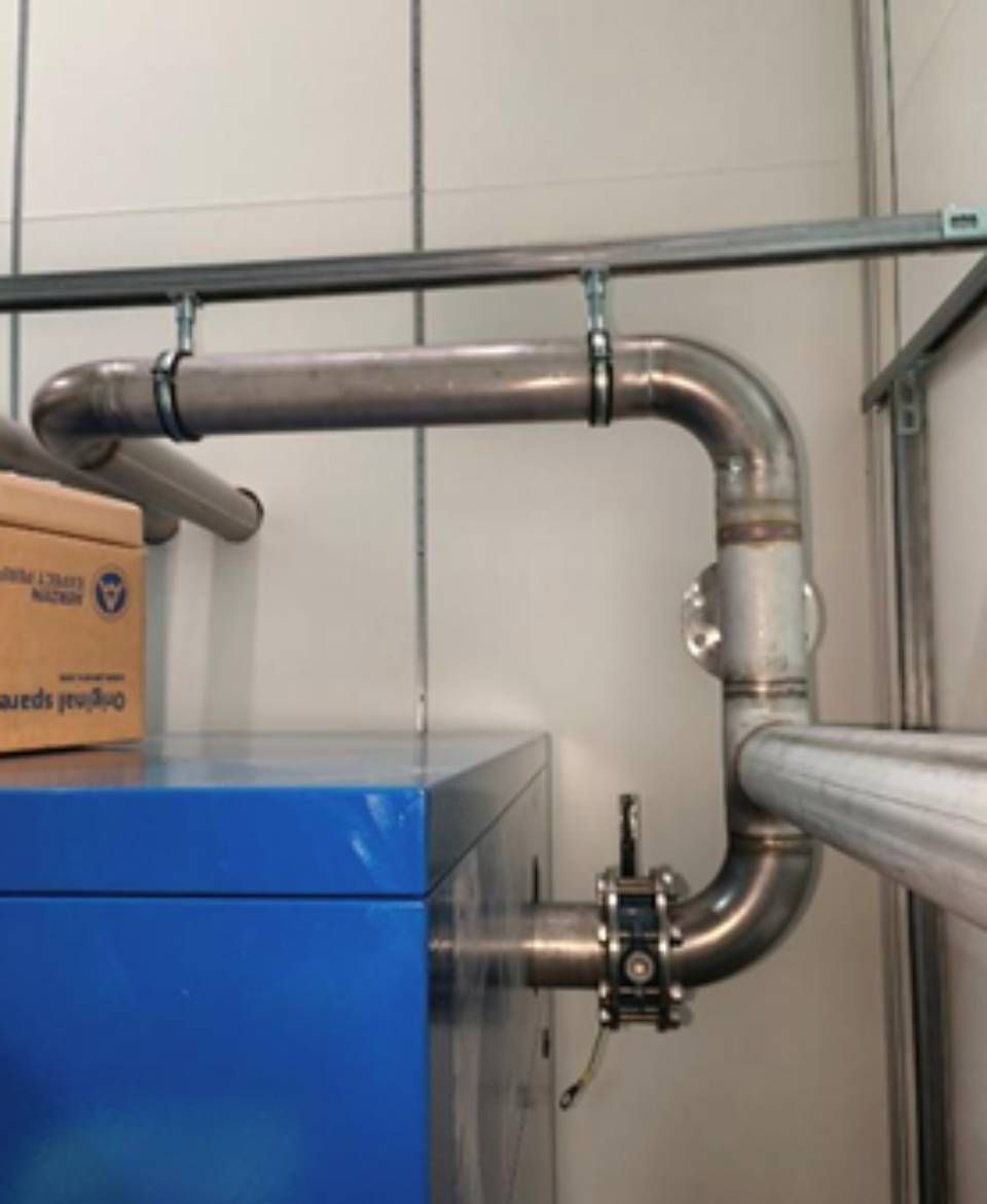 Edelstahlrohre sind mit einer blauen Maschine verbunden und werden von Klemmen an einer weissen Wand gehalten.