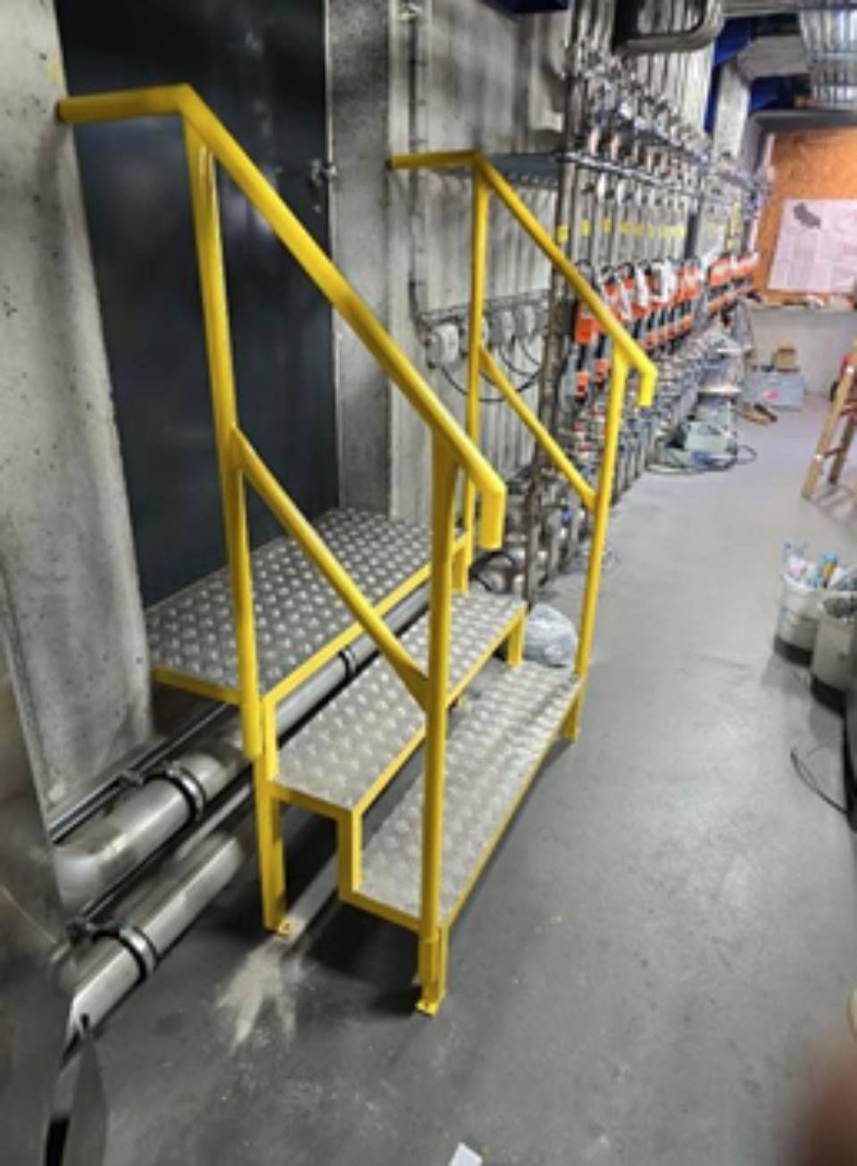 Gelbe Metalltreppe mit Handlauf in einem Industriegebiet.