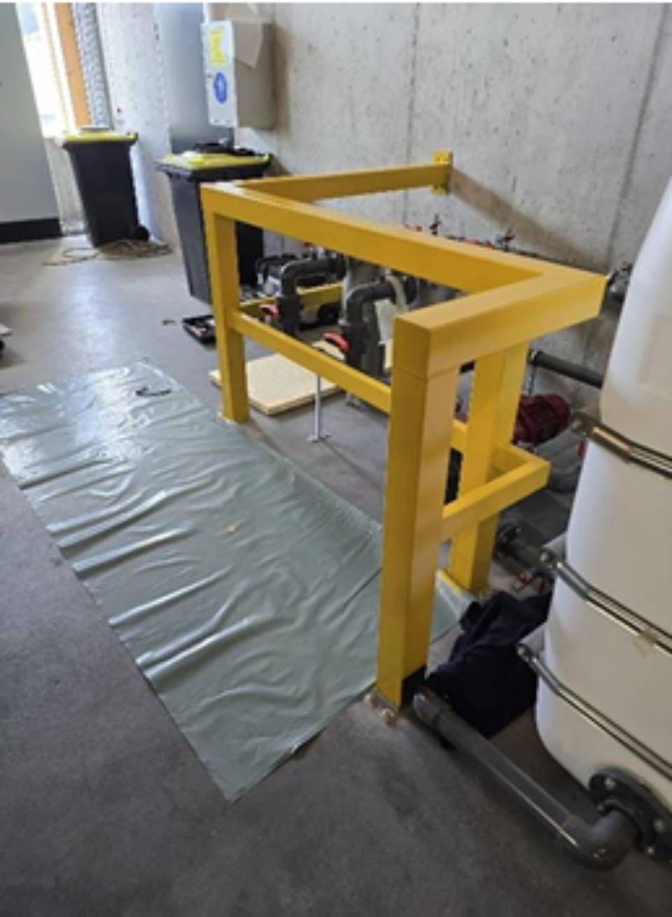 Gelbes Sicherheitsgeländer um die Geräte in einem Technikraum; grauer Bodenbelag, weisser Tank.