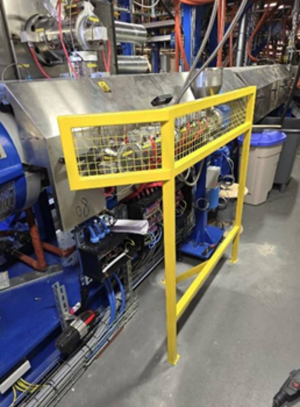 Gelbes Sicherheitsgeländer um Industriemaschinen mit freiliegenden Drähten und elektrischen Bauteilen.