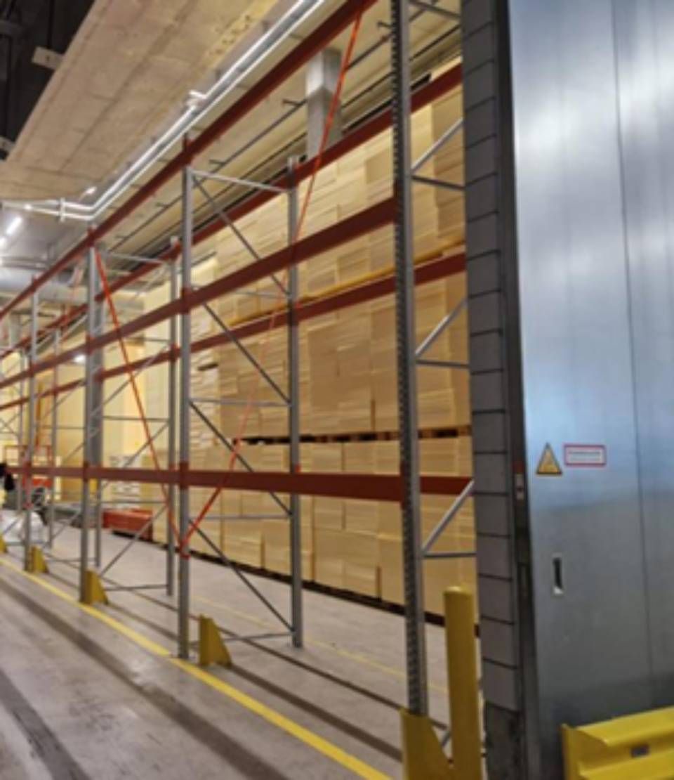 Lagerregale voller Kisten, rotes und graues Metallgestell. Gelbe Bodenmarkierungen.