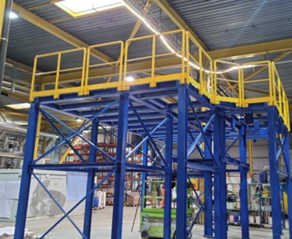 Industrielles Zwischengeschoss in Blau und Gelb mit Sicherheitsgeländern in einer Fabrikumgebung.