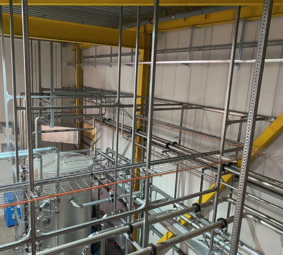 Komplexe industrielle Rohrleitungen und Gerüste in einer Fabrikumgebung, überwiegend graues Metall mit gelben Stützen.