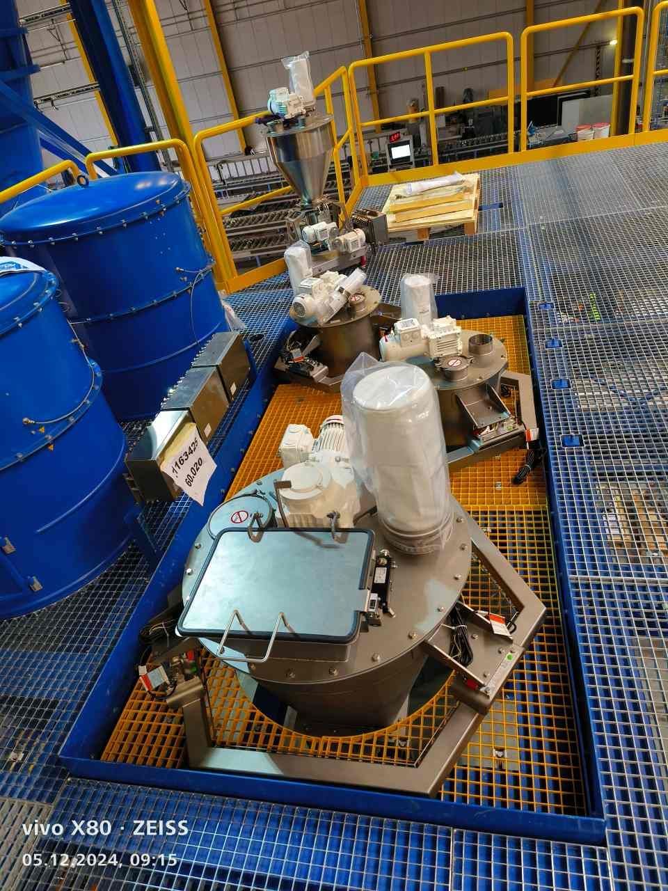 Blaue Industrietanks und Maschinen auf einer Metallgitterplattform.