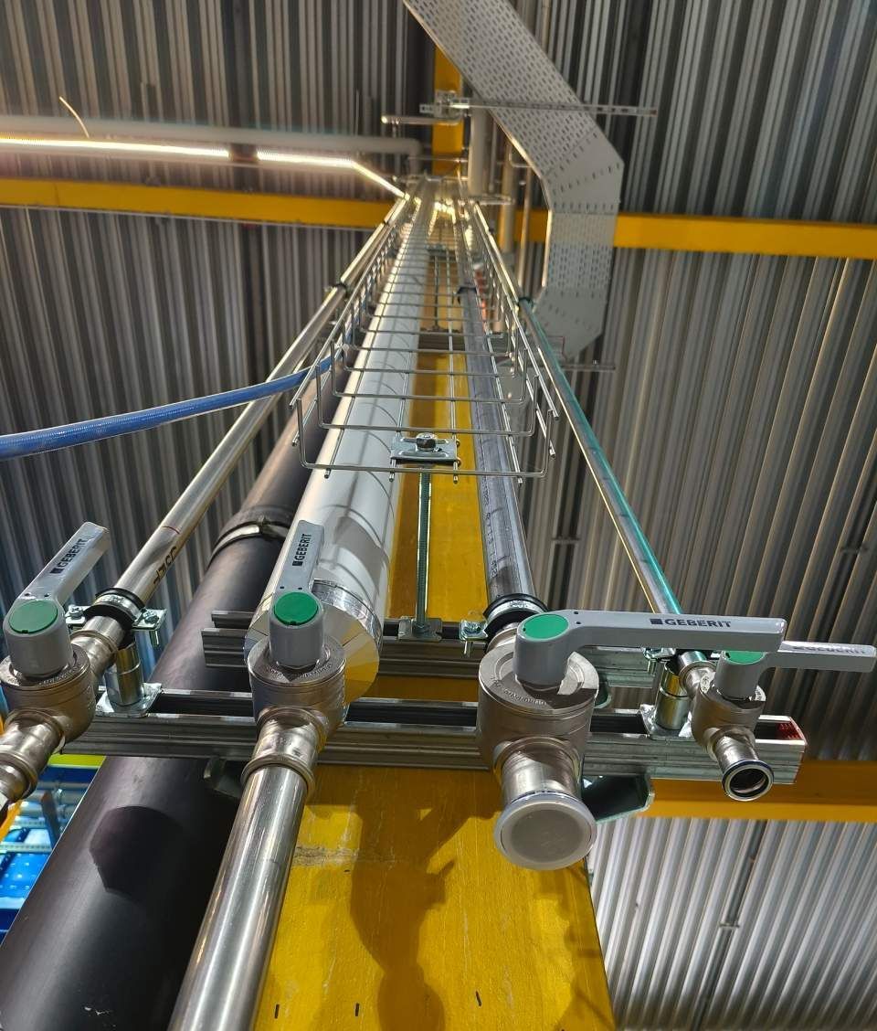 Industrierohre und Ventile sind an einer gelben Stützsäule montiert; eine Leiter ermöglicht den Zugang.