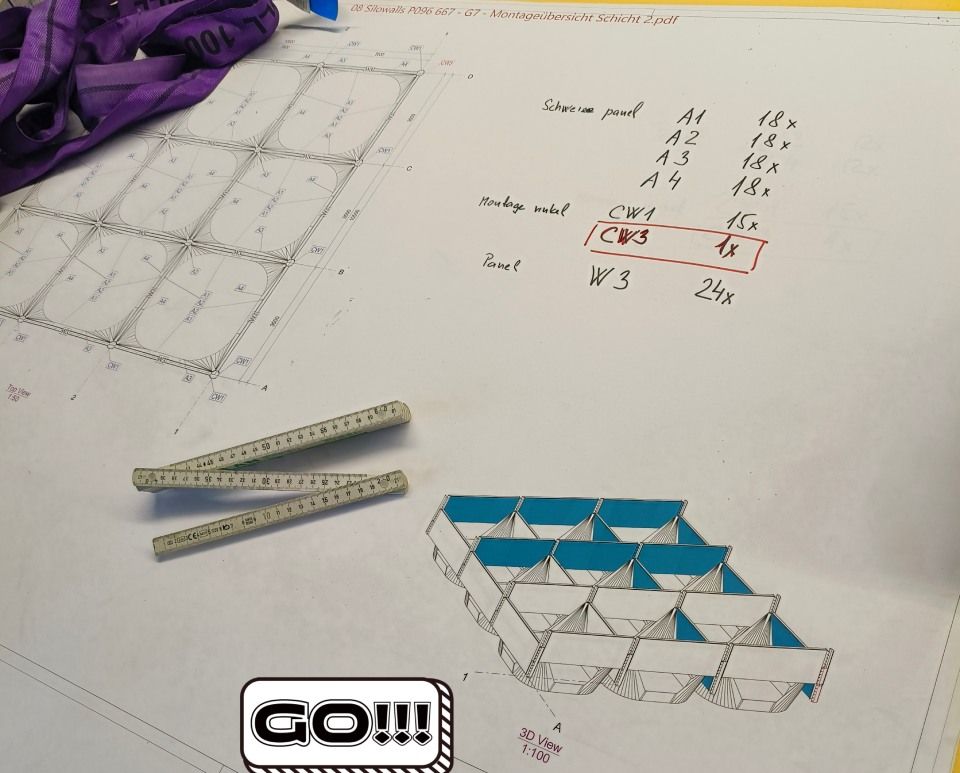 Blau-weisses Bastelmodell mit Bauplan, Messwerkzeugen und handschriftlichen Notizen auf weissem Untergrund.