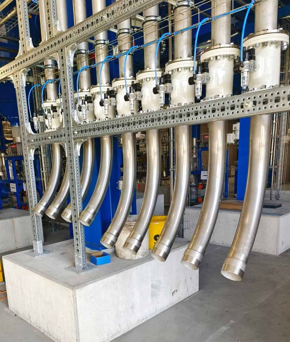 Anordnung von Industrierohren und Maschinen in einer Fabrikumgebung, mit gebogenen Metallrohren.