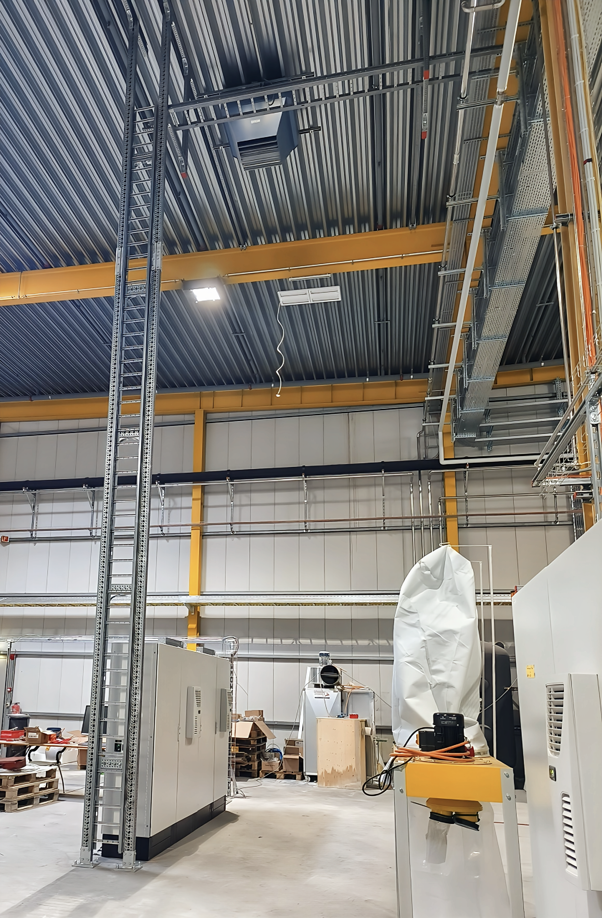 Eine im Bau befindliche, blau lackierte Metallkonstruktion mit bogenförmigen Öffnungen und eckigen Fächern sowie einer kleinen Leiter. Helles Licht von oben.