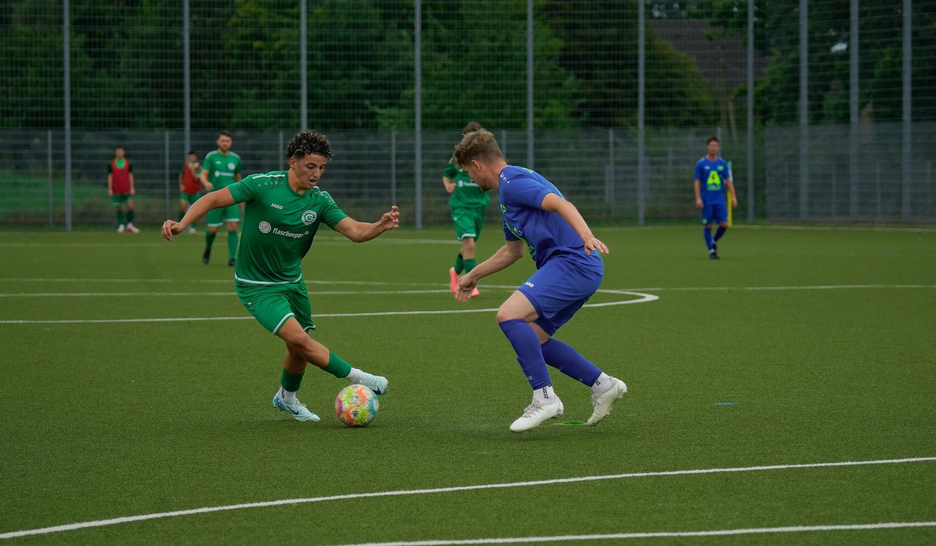 Deux joueurs de football se disputent le ballon sur un terrain vert, l'un en vert et l'autre en bleu.