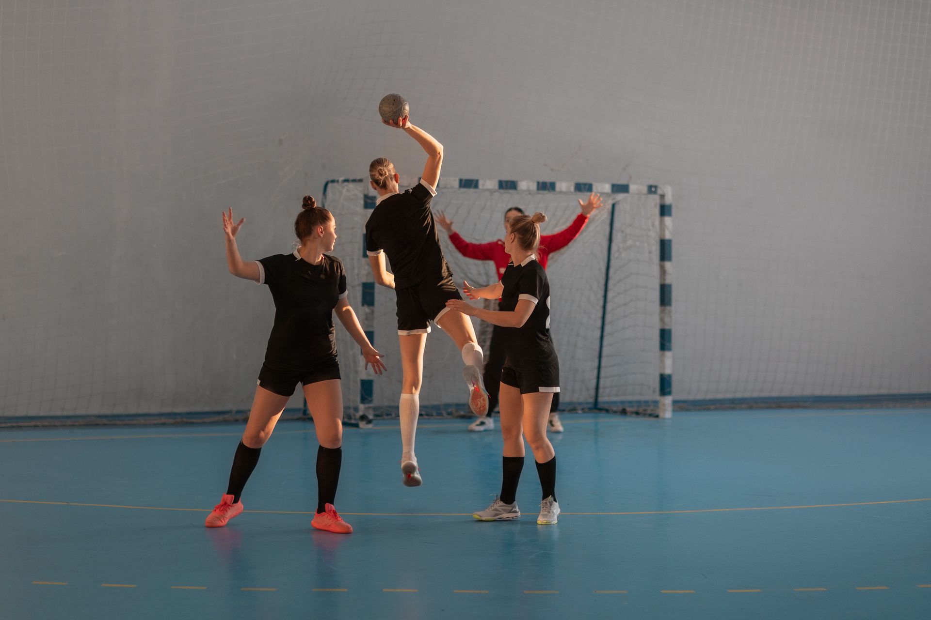 Des joueurs de handball en salle célèbrent un but devant un filet sur un terrain bleu