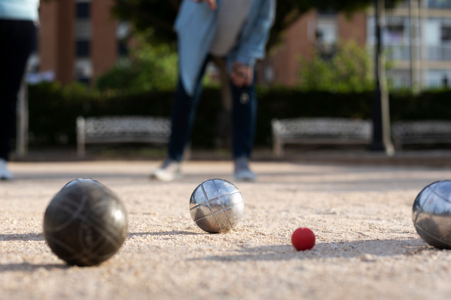 Boules de pétanque sur du gravier, joueurs flous en arrière-plan