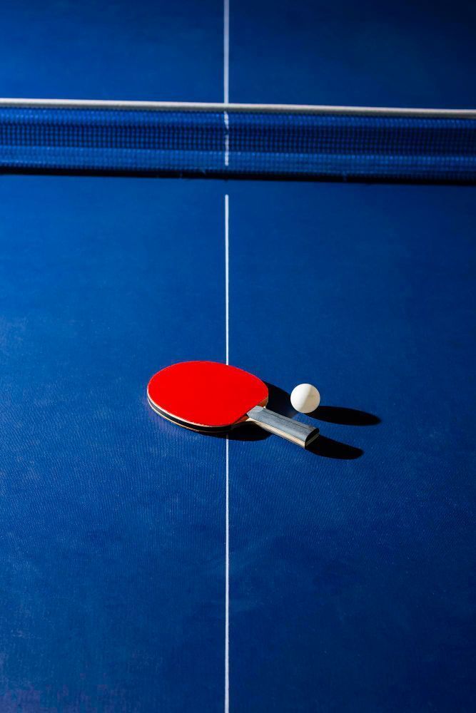 Raquette et balle de ping-pong sur une surface bleue, avec le bord rouge de la raquette visible en dessous.