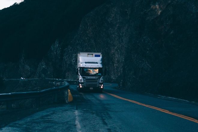 Un camión semirremolque circula por una carretera oscura y sinuosa junto a un acantilado rocoso de montaña.